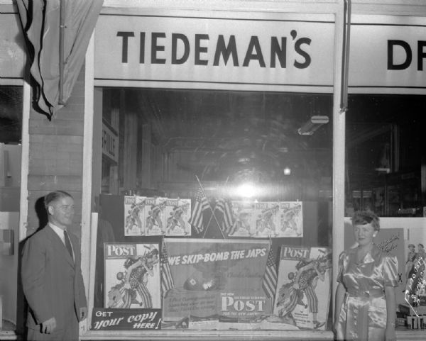 Tiedeman Drug Store, 702 University Avenue, display window showing <i>Saturday Evening Post</i> magazine covers with war theme, with a male and a female employee in the picture.