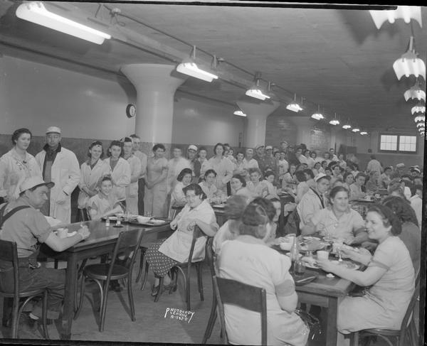 Oscar Mayer Company cafeteria, with workers standing in a food line in the background, and in the foreground people sitting at tables.