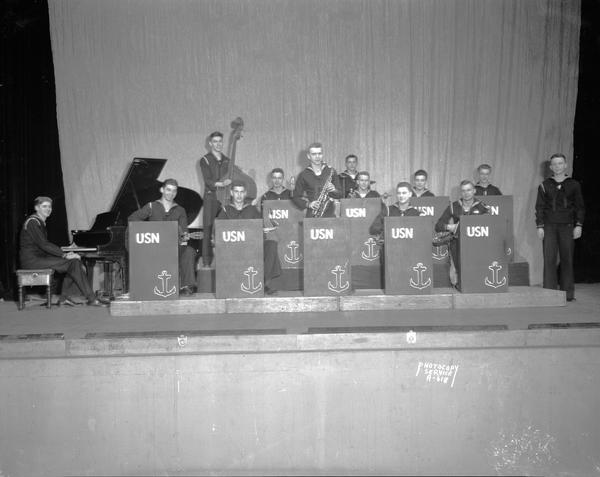 Thirteen members of the Navy band posing on stage.