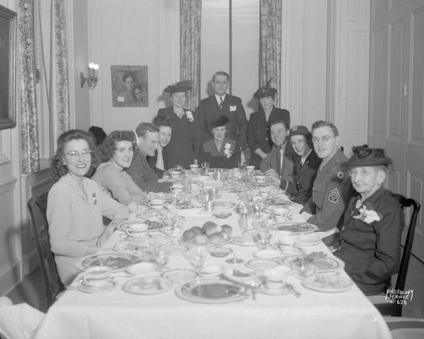 Group portrait of twelve people sitting around the table at the Jeanne Mueller and Leonard Helminiak wedding dinner at the Madison Club.