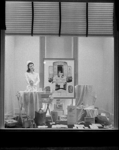 Manchester's, Inc., Baby Development Clinic window display, featuring nurse mannequin bathing a baby mannequin, surrounded by baby products.