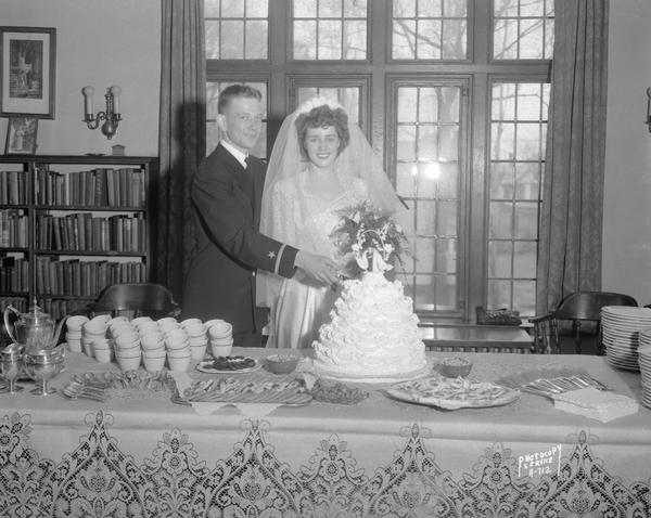 Wedding portrait of Janet Jordan and Ensign William Kommers, taken at St. Francis House, 1001 University Avenue, with bride and groom cutting cake.