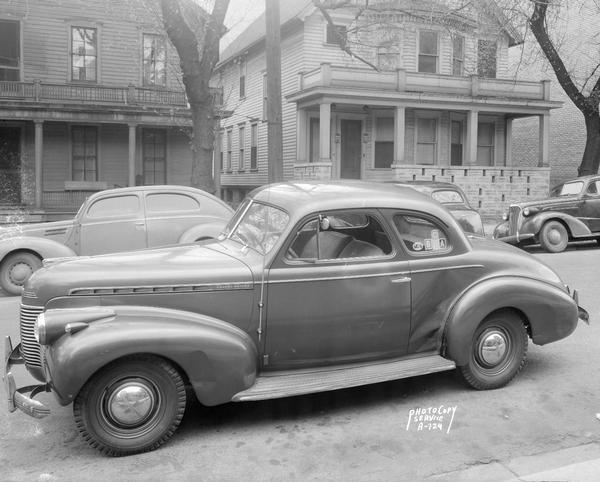 Chevrolet coupe parked on a residential street, showing damage to right side by rear fender.