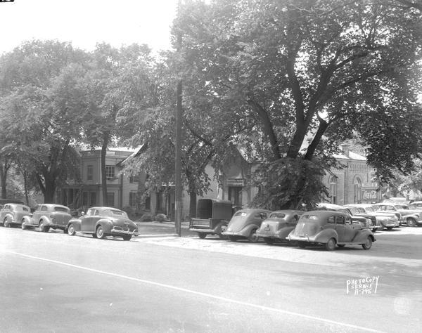 Cars parked in the 200 block of West Washington Avenue. Properties shown are, right to left, Fiore Filling Station parking lot, U.S. Government warehouse (Gates of Heaven Synagogue), Fred Bodenstein residence, and the Davis & Neff Clinic.