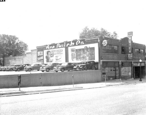 Ace Buick Company sales and service garage, 16 N. Fairchild Street, with Gardner's Purity Bread and Coca-Cola billboards on the side of the building. Automobiles are parked at Fiore filling station parking lot at 202 West Washington Avenue.