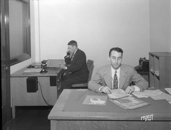 WIBU Radio Station, 114 North Carroll Street, advertising office, showing two men sitting at desks.