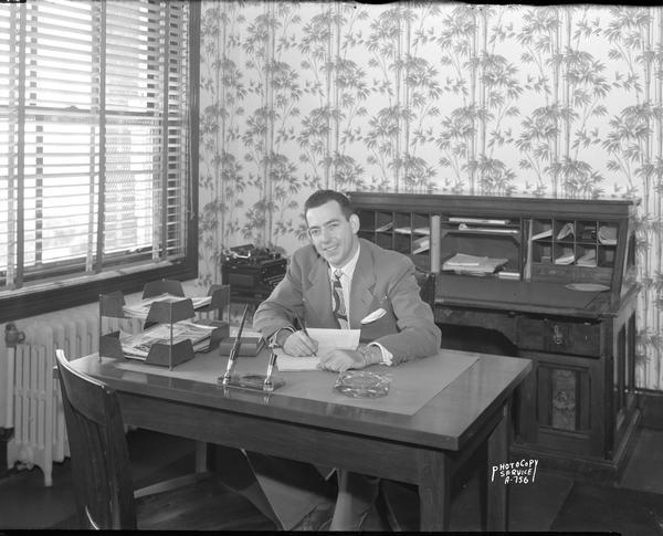Ralph O'Connnor, manager Madison Broadcasting Company, sitting at a desk in WIBU Radio Station office, 114 North Carroll Street.