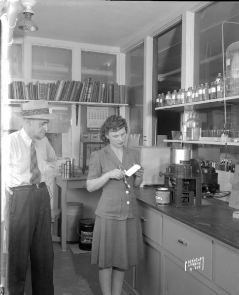 Female chemist using C.M. Ambrose Company paint mixer for testing paint, with a man looking on at the Mautz Paint and Varnish Company, 939 East Washington Avenue.