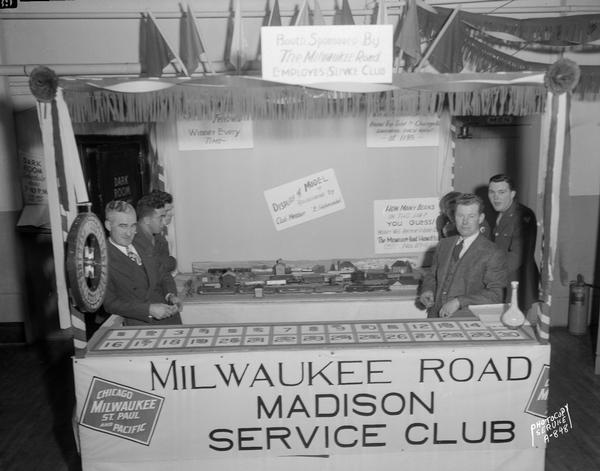 Booth at the U.S.O. Carnival sponsered by the Milwaukee Road Employees Service Club, featuring games of chance and a model train set-up.
