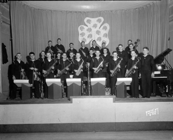 United States Navy Band on stage, decorated with shamrocks, at the University of Wisconsin Memorial Union showing members of the band with their instruments.