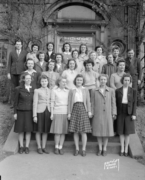 Group portrait of University of Wisconsin-Madison Library School students and staff taken in front of their classroom building, 811 State Street. The man on the right in the back row is George C. Allez, Director of the Library School, and the woman next to him is Alma Runge, an instructor.