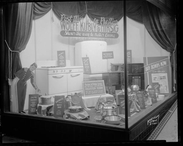 Display in left window of future post-war products including appliances manufactured by Toastmaster, All America, General Electric, Proctor, Sunbeam, Steam-o-matic, Universal, Eldridge, and Swing Away. "Post War as in Pre War Wolff Kubly & Hirsig Shows the Way to Better Living," 17 South Pinckney Street.
