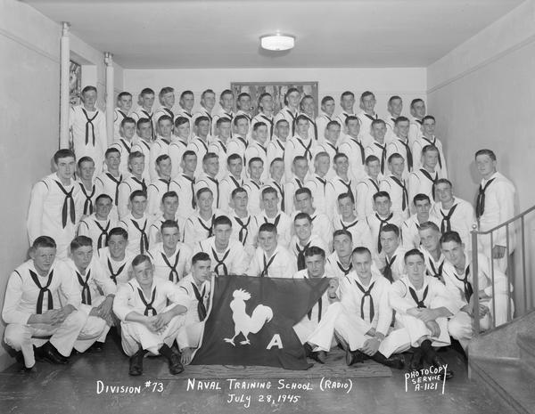 Group portrait of U.S. Naval Training School (Radio), Division #73, trainees at University of Wisconsin, Madison with banner depicting a roster and the letter "A".