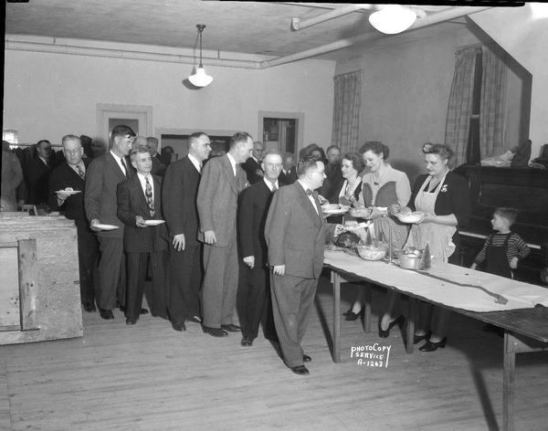 Milwaukee Road Service Club family party at E.R.A. Hall, with seven male officers in line being served food by three women, with a small boy looking on.
