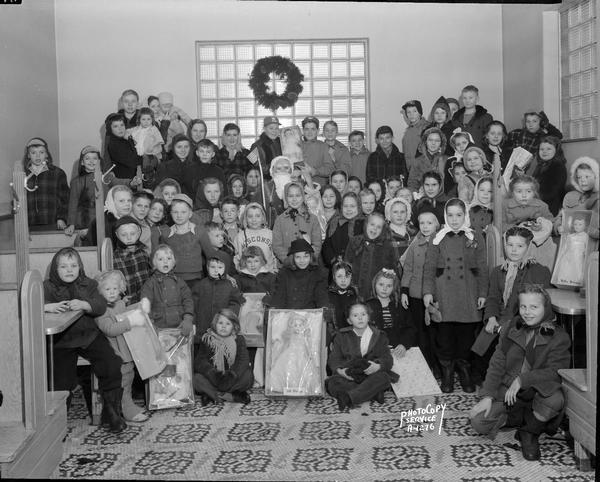 Group portrait of children wearing winter coats and boots, who have received Christmas gifts at a party sponsored by the Rennebohm's drug stores.
