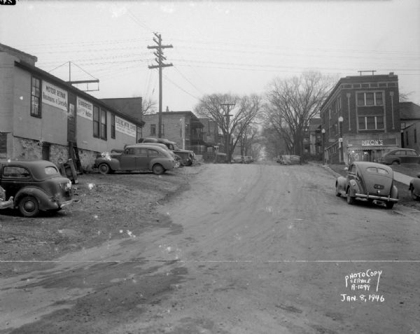 South Hancock Street scene looking north uphill across East Wilson Street, taken at site of Reynolds Bus accident. Businesses shown include the Electric Motor Service at 323 East Wilson Street and Dizon Men's Clothing Store at 402 East Wilson Street. Residences shown include houses in the 100 block of South Hancock Street.