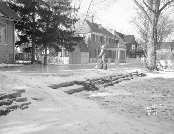 Arnold S. Zander sweeping ice skating rink at 175 Virginia Terrace. Photograph taken for AFSCME American Federation of State County and Municipal Employees of which Mr. Zanders was president. View includes snow slide, playhouse/warming house next to the rink, and three houses on Virginia Terrace.