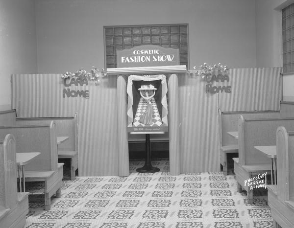 Backdrop for a Cara Nome brand cosmetics in the restaurant portion of Rennebohm Drug Store #12, 2526 Monroe Street. There are food service booths in the foreground on the left and right.