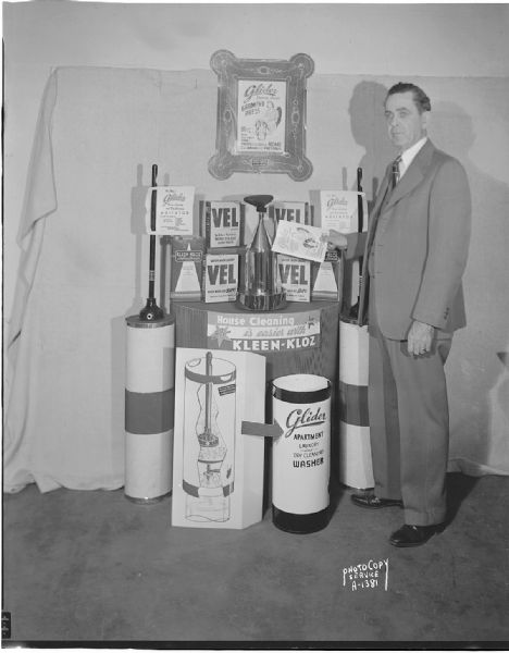 Mr. Mullarkey (probably Leo R. Mullarkey) standing beside Glider Home Laundry and Dry Cleaning Agitator, Washer and steam garment press with Vel Colgate soap and Kleen Kloz dry cleaning fluid.