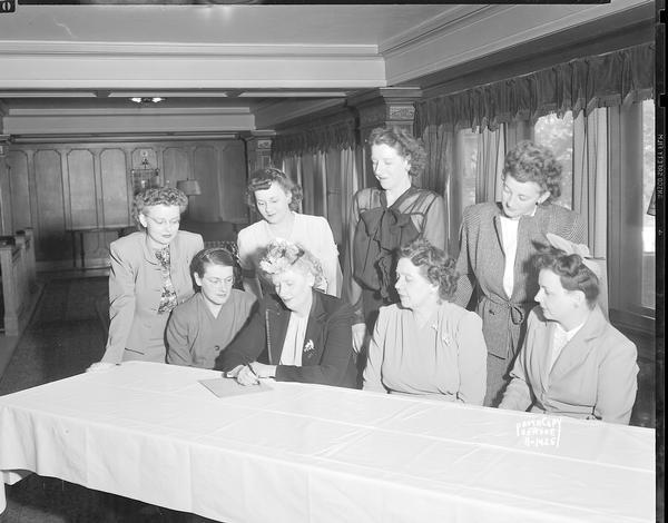 Group portrait of CUNA (Credit Union National Association) Womens's Convention Luncheon Committee at Loraine Hotel, composed of eight women sitting and standing behind a table.