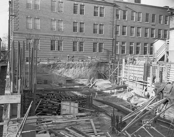 Wisconsin Telephone Co. building site, 122 West Main Street, looking north with construction workers in unfinished basement. Also shows side of Wisconsin Telephone Company building, 17 South Fairchild Street. Building constructed by J. H. Findorff & Son Inc. construction company.