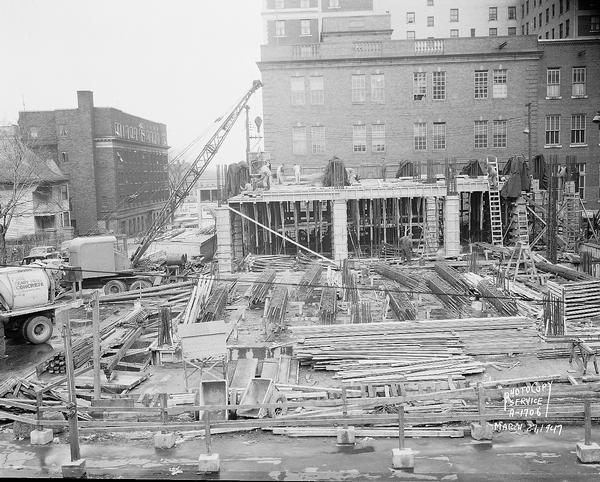 Wisconsin Telephone Co. building site, 122 West Main Street, looking north across basement and first floor with part of the second floor under construction. Also shows side views of YMCA, 207 West Washington Avenue and telephone building, 17 South Fairchild Street and construction crane and cement mixer. Building constructed by J. H. Findorff & Son Inc. construction company.