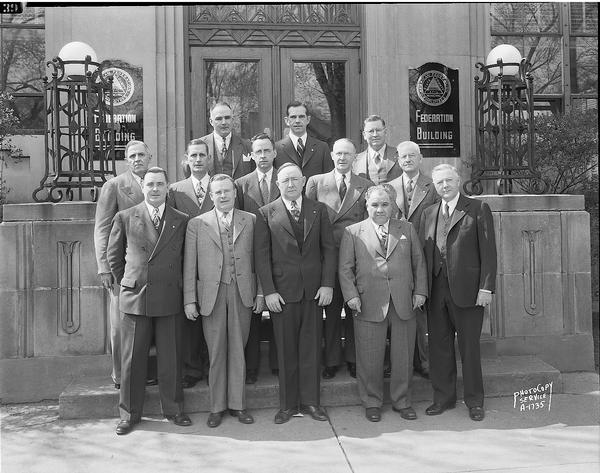 A group portrait of thirteen male State representatives of the American Federation of State, County and Municipal Employees, taken in front of the Federation Building, 448 West Washington Avenue.