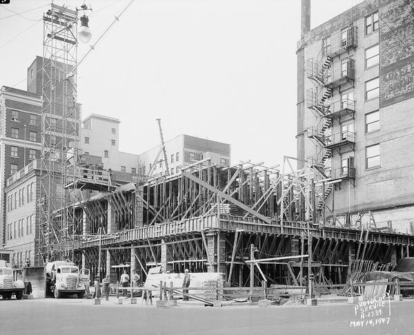 Wisconsin Telephone Co. building site, 122 West Main Street, looking north across South Fairchild at scaffolding for first floor and second floors under construction. Also shows telephone building, 17 South Fairchild Street and tower crane, two trucks and back sides of Loraine Hotel and Park Hotel. Building constructed by J.H. Findorff & Son Inc. construction company.