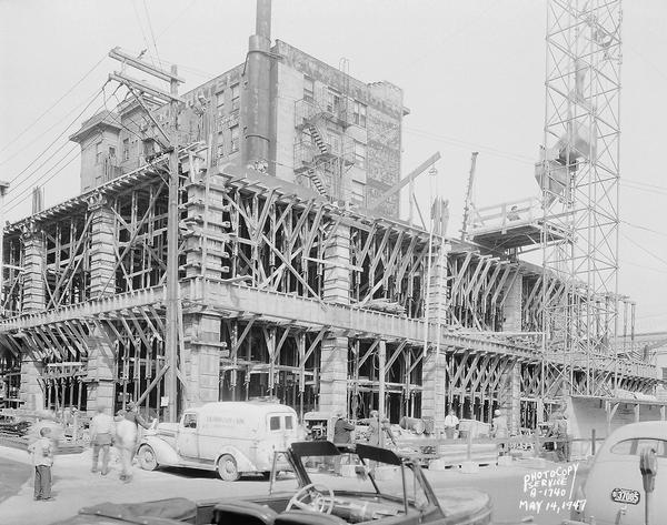 Wisconsin Telephone Co. building site, 122 West Main Street, looking south east across South Fairchild Street at scaffolding for first floor and second floors under construction. Also shows side view of Park Hotel and tower crane, Findorff panel truck and part of a convertible automobile. Building constructed by J.H. Findorff & Son Inc. construction company.
