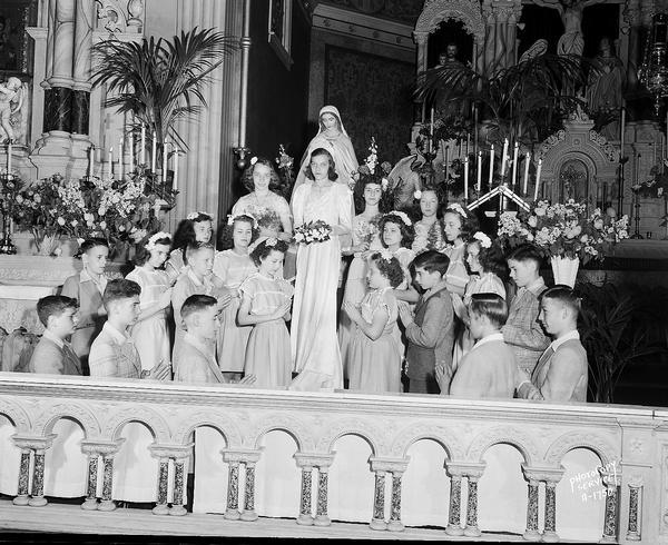 Interior of Holy Redeemer Catholic Church, 128 West Johnson Street, May Queen (Virgin Mary) crowning ceremony. Shows the coronation Queen accompanied by three attendants, and children praying.