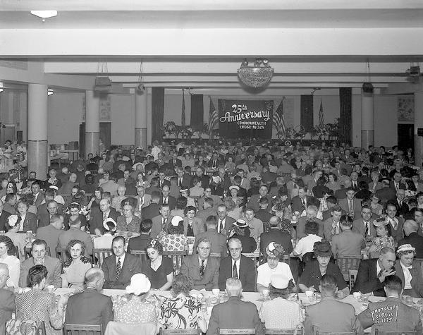 Masonic Commonwealth Lodge No. 325 twenty-fifth anniversary dinne. Wide angle view showing masons and their wives sitting at tables, and floral decorations on the speakers table.