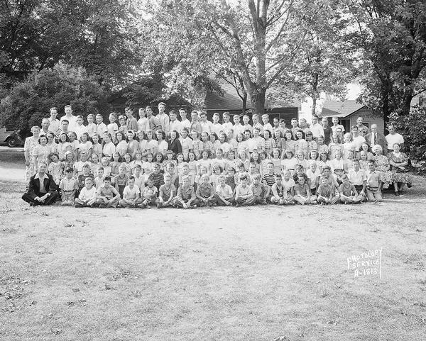 Group portrait of children and adults at a Free Methodist Church bible camp, with cabins in the background, taken for Reverend James Shaw. The site had been the Hallelujah Camp Grounds run by Rev. Clement H. "Jack" Linn in the 1920s and 1930s.