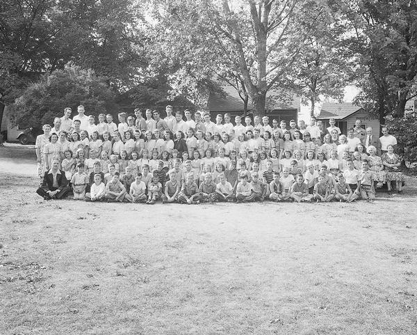 Outdoor group portrait of children and adults at a bible camp, with cabins in the background, taken for Reverend James Shaw. The site was the Hallelujah Camp Grounds run by Rev. Clement H. Jack Linn in the 1920s and 1930s.