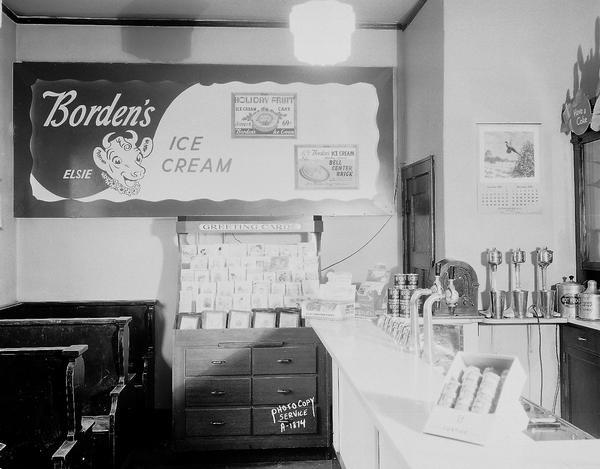 Hudson Park Pharmacy, 2337 Atwood Avenue, interior view of soda fountain, with a display of greeting cards and booths, and a poster for "Elsie" Borden's Ice Cream.