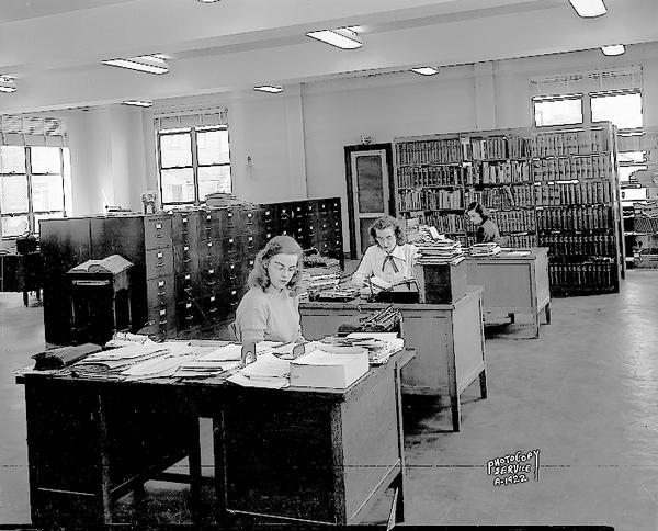 Three women clerks sitting at desks in the library in the American Federation of State, County and Municipal Employees Building, 448 West Washington Avenue.