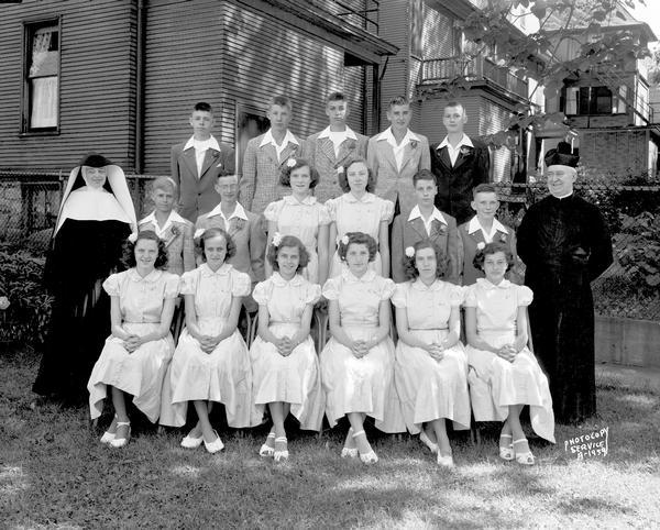 Group portrait of Holy Redeemer graduation class taken outside of the church at 140 West Johnson Street. Includes eight girls, nine boys, one nun and one priest.