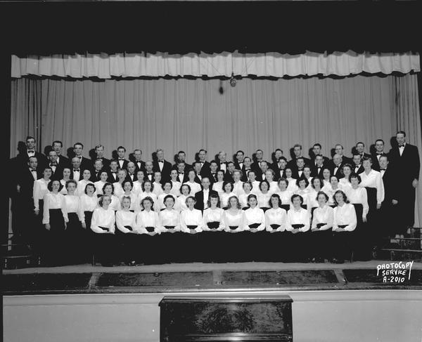 A group portrait of Philharmonic Chorus with the director on stage at West High School, 30 Ash Street.