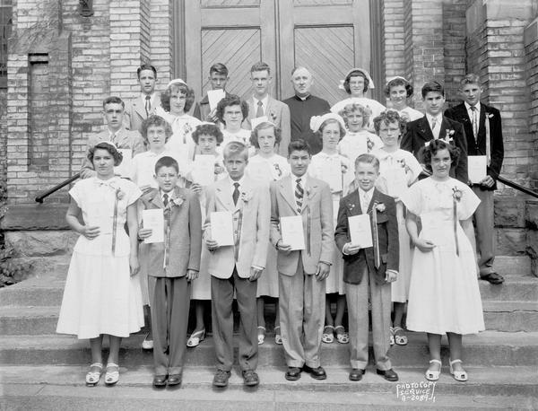 Group portrait of St. Patrick's School graduation class with priest taken on the steps of the church, 410 East Main Street.