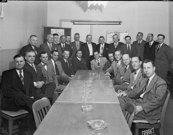 Group portrait of 25 Ohio Chemical & Surgical Equipment Company salesmen seated and standing around a table, 1400 East Washington Avenue.