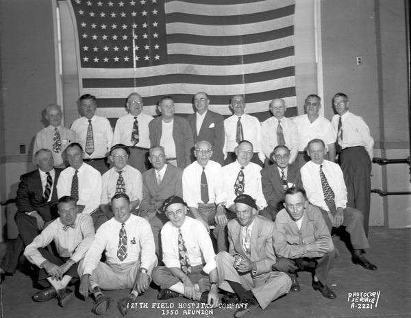 Group portrait of the 127th Field Hospital company reunion, with a large United States flag in the background.