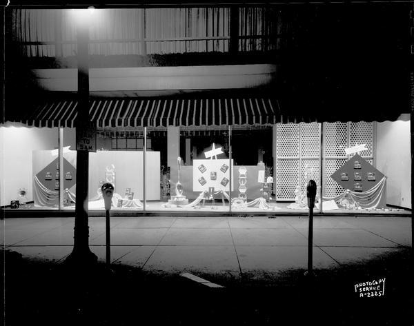 A window display at Manchester's, Inc., 2 East Mifflin Street, taken from the street showing sidewalk and parking meters, featuring Wallace, International and Lunt sterling silverware.