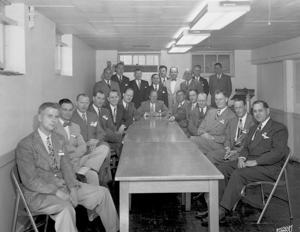 Group portrait of 22 salesmen for Ohio Chemical & Surgical Company sitting and standing around a table in the basement of old Fuller & Johnson building, 52 North Dickinson Street.