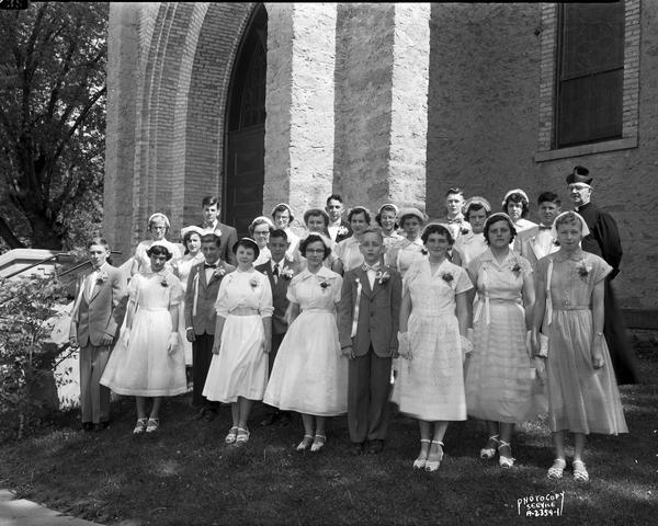 St. Francis Xavier Catholic School graduating class, with priest, taken in front of the church.