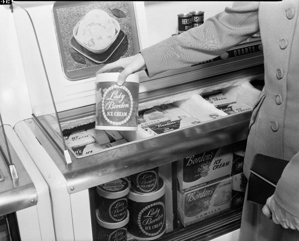 Borden's ice cream in display case, with a person (hand and arm only showing) lifting a carton of ice cream from case, taken for a TV ad.