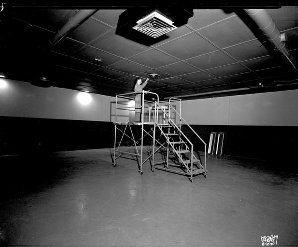 Man standing on a platform ladder adjusting a ceiling ventilator in the testing room at W.R. Carnes Company, wide angle view.