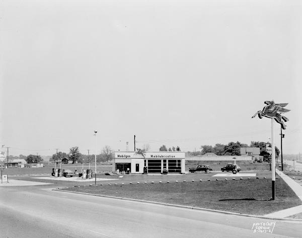 Daytime view of Robert Bloxxom's Mobil gas station, 3702 East Washington Avenue and Highway 51. Includes the Mobil red horse on a pole. Background includes Klein's Greenhouse at 3758 East Washington Avenue.