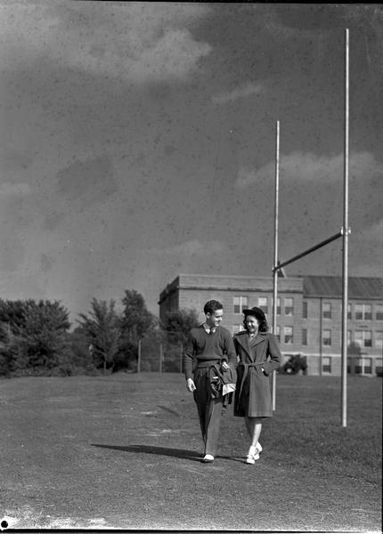 Two high school students (boy and girl) walking on football field. "Hundred to One" It's for you! Manchester's new Fall merchandise sale. Advertisement says: "The Teen Shop on Third Floor is a popular spot for clothes-conscious high school girls."
