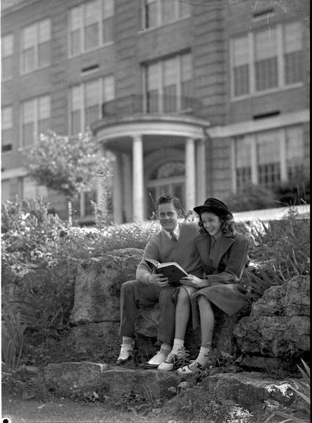 Teenagers modeling for the Teen Shop at Manchester's. They are sitting outdoors looking at a book. A college building is in the background.