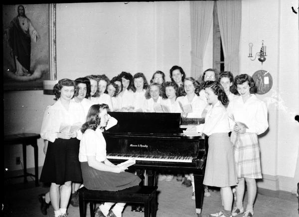 Large group of Edgewood students standing around a piano, with one student sitting on the piano bench.