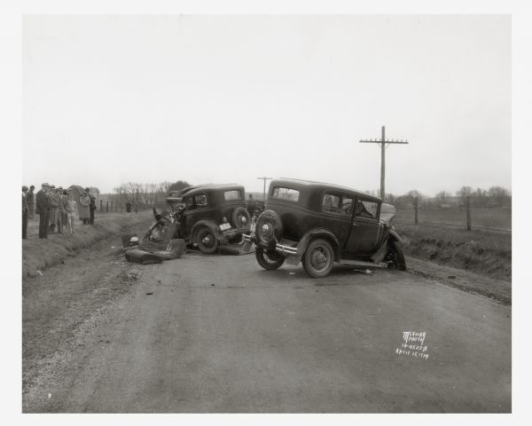 Onlookers surveying damage from a fatal two-car collision. The view is looking south on County Trunk Highway M, between Speedway Road and Middleton. In the accident Leo Maly was killed, and his wife, Edna, and son, Paul, and brother-in-law, Raymond Frisch, were injured. August Sternhagen, from Mazomanie, was also injured. This photograph was taken by news photographer Angus McVicar. His collection in the Archives, as well as those of numerous other Wisconsin newspaper photographers, testify to both the frequency and destructiveness of automobile accidents even during the automobile's early days.